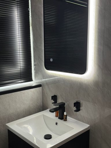 Black framed LED backlit bathroom mirror with matte black basin tap and wall-mounted fittings installed by bathroom fitters in Kent
