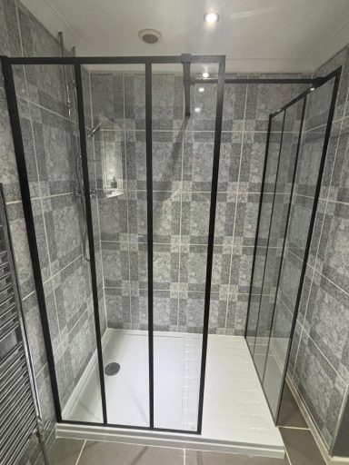 Black framed walk-in shower enclosure with grey patterned tiles and white shower tray fitted by bathroom fitters in Kent