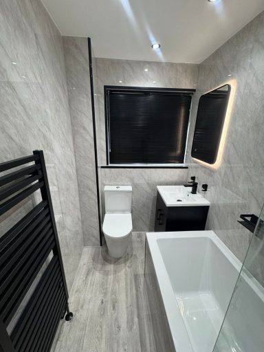 Modern bathroom installation with grey marble-effect panels, black heated towel rail, freestanding bath and LED mirror completed by plumbers